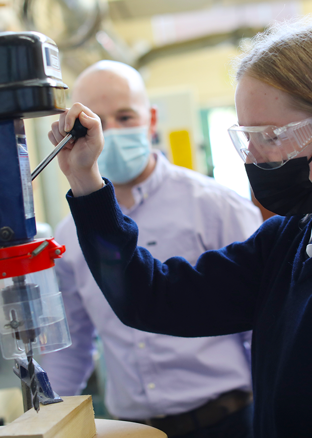 Female student using equipment in the construction room with teacher supervising